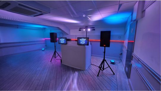 Heard The Beat DJ booth setup in a modern venue with ambient blue and purple lighting, dual display screens, and PA speakers on stands