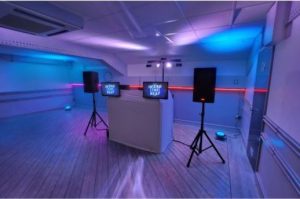 Heard The Beat DJ booth in a blue and purple lit room with dual screens, professional speakers, and floor uplighting