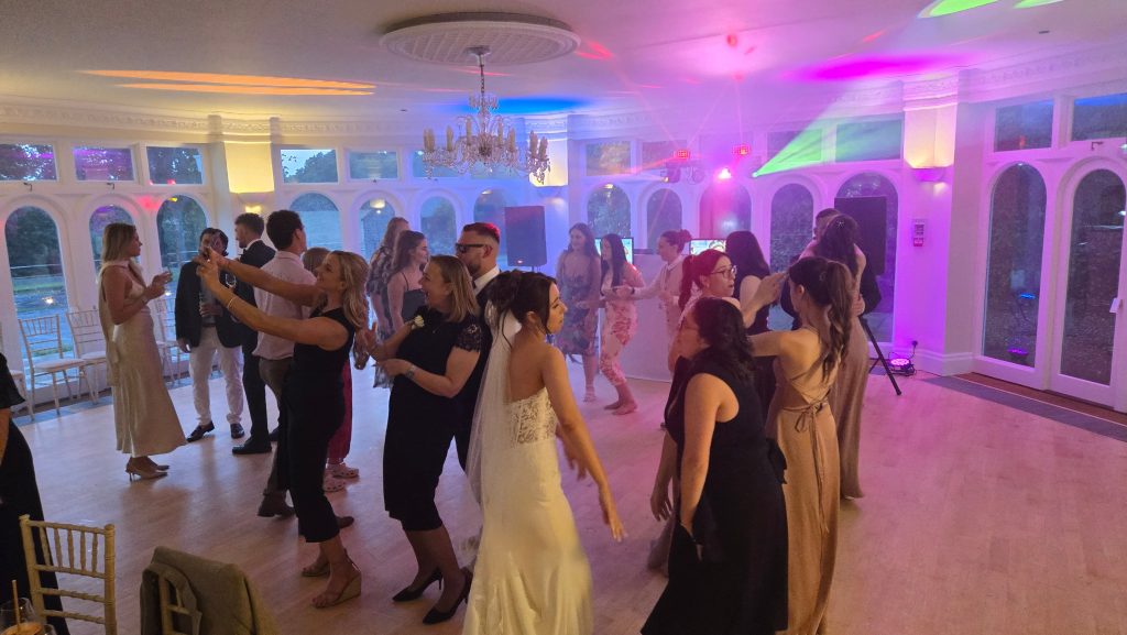 Guests dancing and enjoying the evening on the dance floor at a wedding reception with colourful DJ lighting and a chandelier overhead