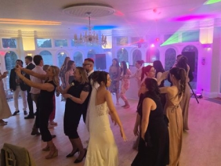 Guests dancing and enjoying the evening on the dance floor at a wedding reception with colourful DJ lighting and a chandelier overhead