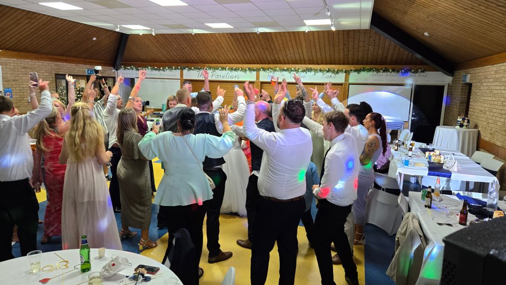 Wedding guests raising their hands on the dance floor at the end of the night at The Pavilion Farlington, Portsmouth, with DJ lights and celebration vibes