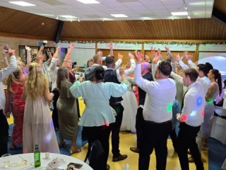 Wedding guests raising their hands on the dance floor at the end of the night at The Pavilion Farlington, Portsmouth, with DJ lights and celebration vibes