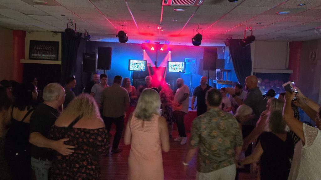 Guests dancing at The Royal Naval Association Gosport in front of a professional DJ booth with vibrant lighting.