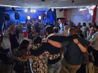 Guests arm in arm enjoying a lively circle dance at The Royal Naval Association Gosport with DJ music and lighting.
