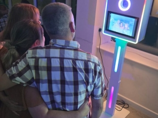 Three people with arms around each other posing in front of a glowing LED photo booth with an umbrella light.