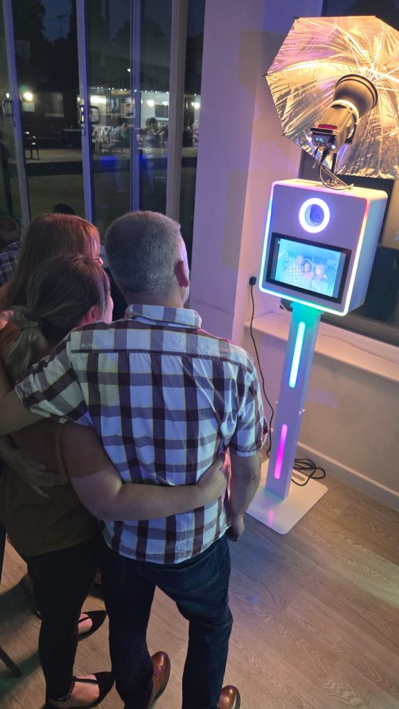 Three people with arms around each other posing in front of a glowing LED photo booth with an umbrella light.