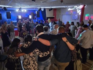 Guests arm in arm enjoying a lively circle dance at The Royal Naval Association Gosport with DJ music and lighting.