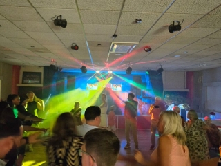 Guests dancing on the floor with vibrant DJ lighting effects and lasers filling the room.