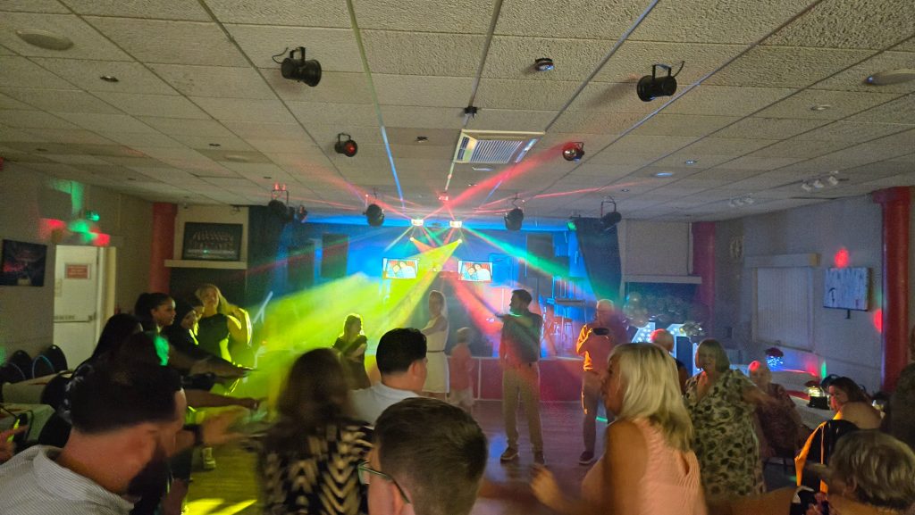 Guests dancing on the floor with vibrant DJ lighting effects and lasers filling the room.