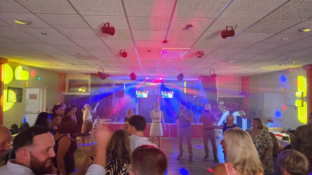 Packed dance floor with colourful beams and spotlights creating a lively party vibe.