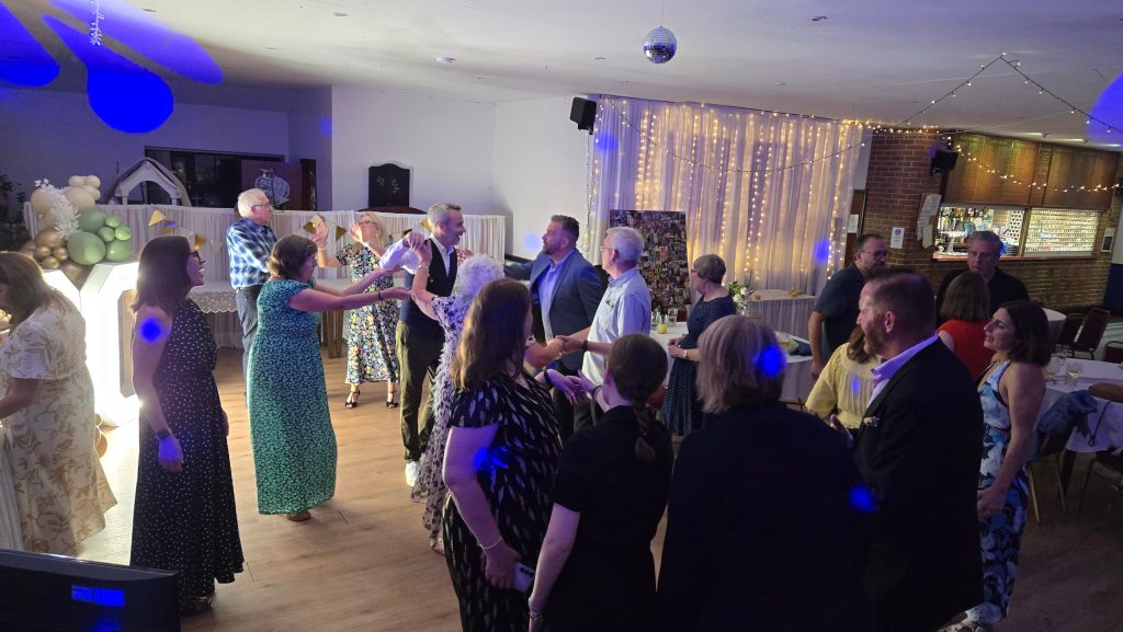 Group of guests holding hands and dancing together on the dance floor with decorative lighting.