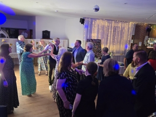Group of guests holding hands and dancing together on the dance floor with decorative lighting.