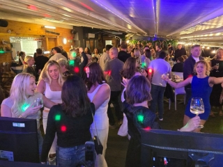 Large crowd celebrating at a party in a stylish bar venue with disco lighting and dancing.