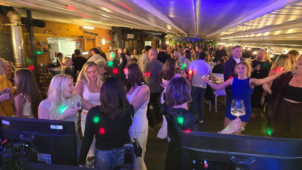 Large crowd celebrating at a party in a stylish bar venue with disco lighting and dancing.