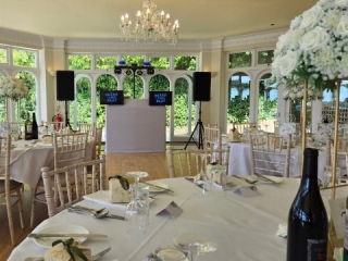 Beautifully decorated wedding reception room with round tables, floral centrepieces, chandeliers, and a professional Heard The Beat DJ booth with twin screens and speakers.