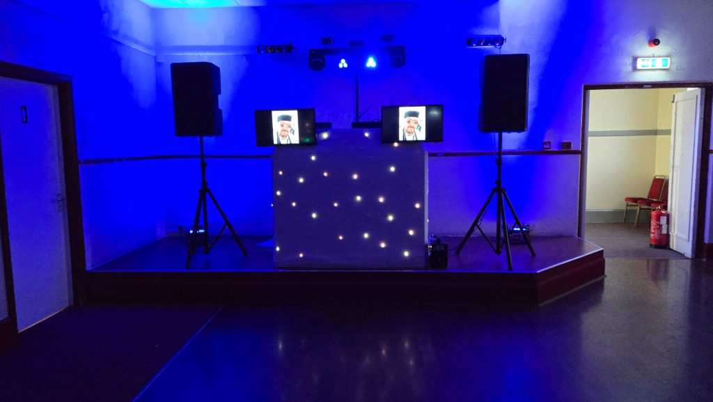 DJ setup with blue lighting effects, twin monitors, and starlit DJ booth ready for an evening event.