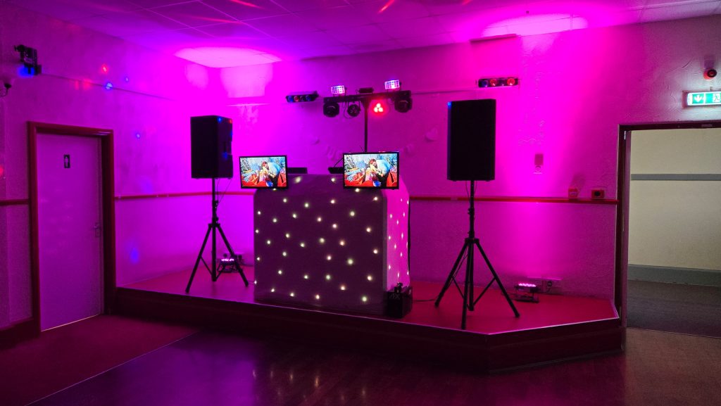 Pink and purple DJ lighting display with starlit booth, dual screens, and full sound system setup for a wedding party.
