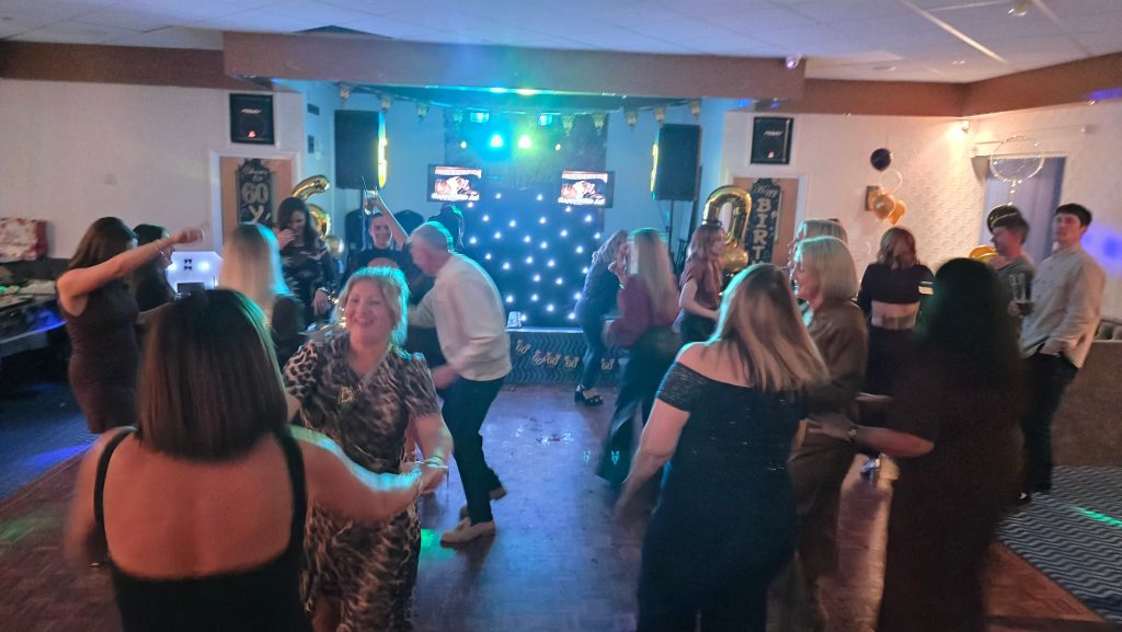 Guests dancing near the DJ booth at Jo’s 60th birthday party at Broad Oak Social Club in Portsmouth.
