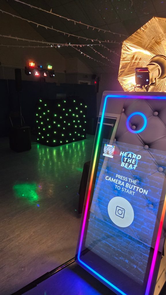 DJ and photo booth setup for an event, featuring a Magic Mirror photo booth and professional lighting by Heard The Beat