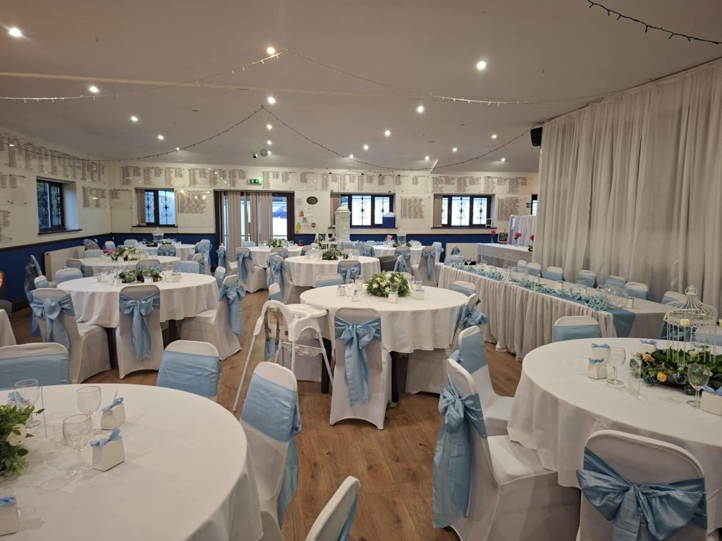 Wedding reception setup at Southsea Golf Club in Portsmouth with round tables, white chair covers and blue sashes, ready for an evening celebration.