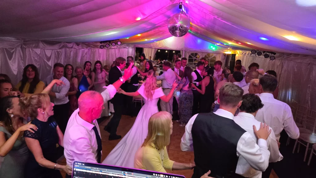 Bride and wedding guests dancing under colourful DJ lighting inside a marquee
