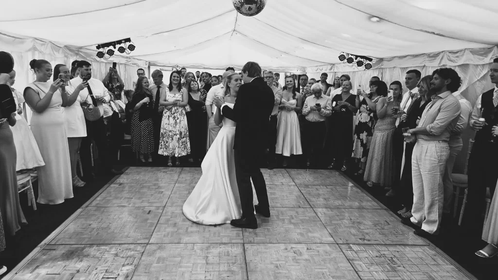 Bride and groom sharing their first dance inside a marquee surrounded by wedding guests
