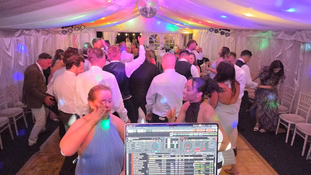 Wedding guests dancing under colourful DJ lighting in the marquee at Portsmouth Distillery